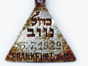  Das Amulett des Frankfurter Mädchens Karolin Cohn, geb. am 3. Juli 1929. Darüber auf Hebräisch: "Mazel tov" ("Viel Glück"). Einen sehr ähnlichen Anhänger besaß auch die im gleichen Jahr geborene Anne Frank. Das Amulett des Frankfurter Mädchens Karolin Cohn, geb. am 3. Juli 1929. Darüber auf Hebräisch: "Mazel tov" ("Viel Glück"). Einen sehr ähnlichen Anhänger besaß auch die im gleichen Jahr geborene Anne Frank.